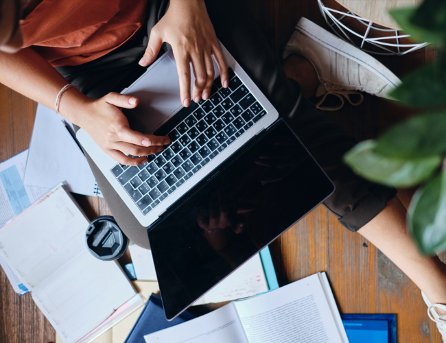 student typing on laptop in online course with books and notes scattered around